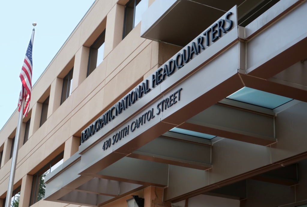 El exterior del edificio de la sede del Comité Nacional Demócrata, que presenta una bandera estadounidense en un asta y una prominente marquesina moderna que muestra el texto "Democratic National Headquarters" y "430 South Capitol Street".