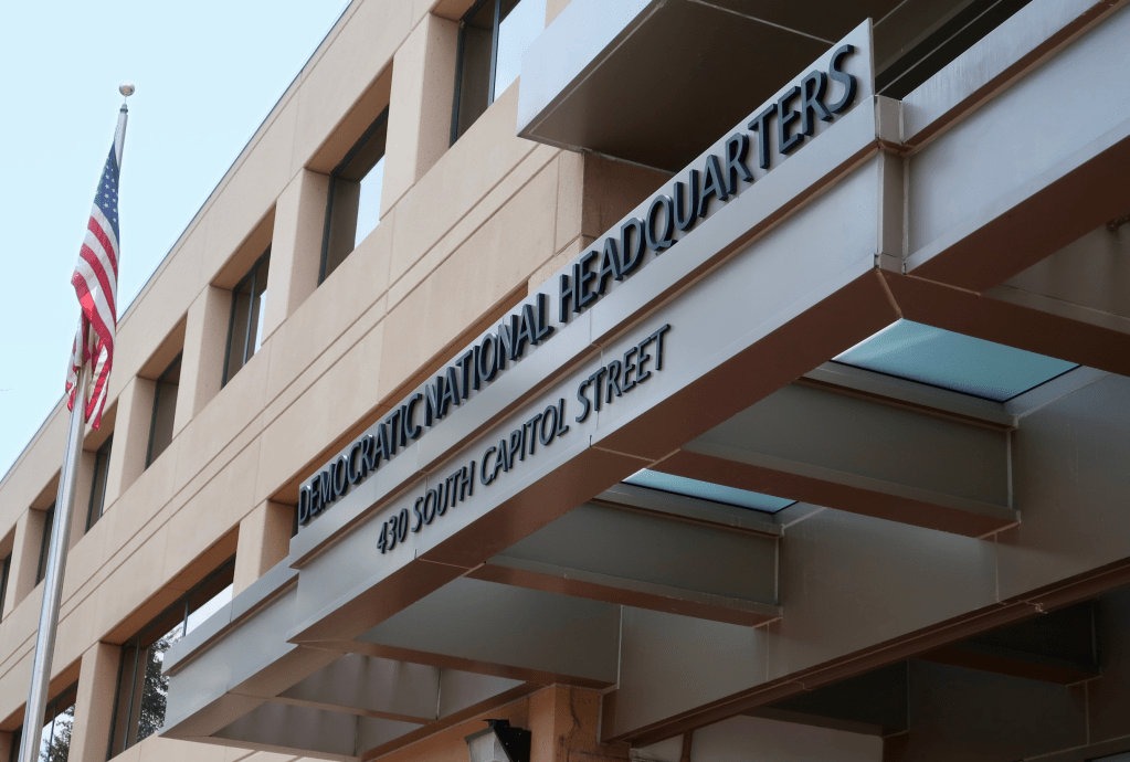 The exterior of the Democratic National Committee headquarters building, featuring an American flag on a flagpole and a prominent modern awning displaying the text "Democratic National Headquarters" and "430 South Capitol Street".